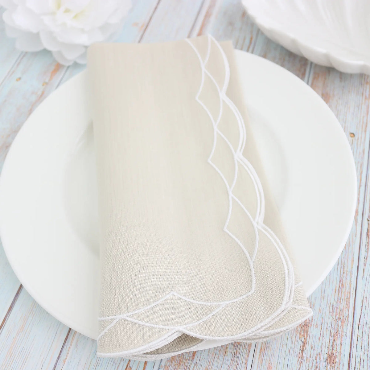 White plate with gold cutlery on a white background, featuring a Fog Beige folded scalloped dinner napkin and the brand 'Cora's Linens'.