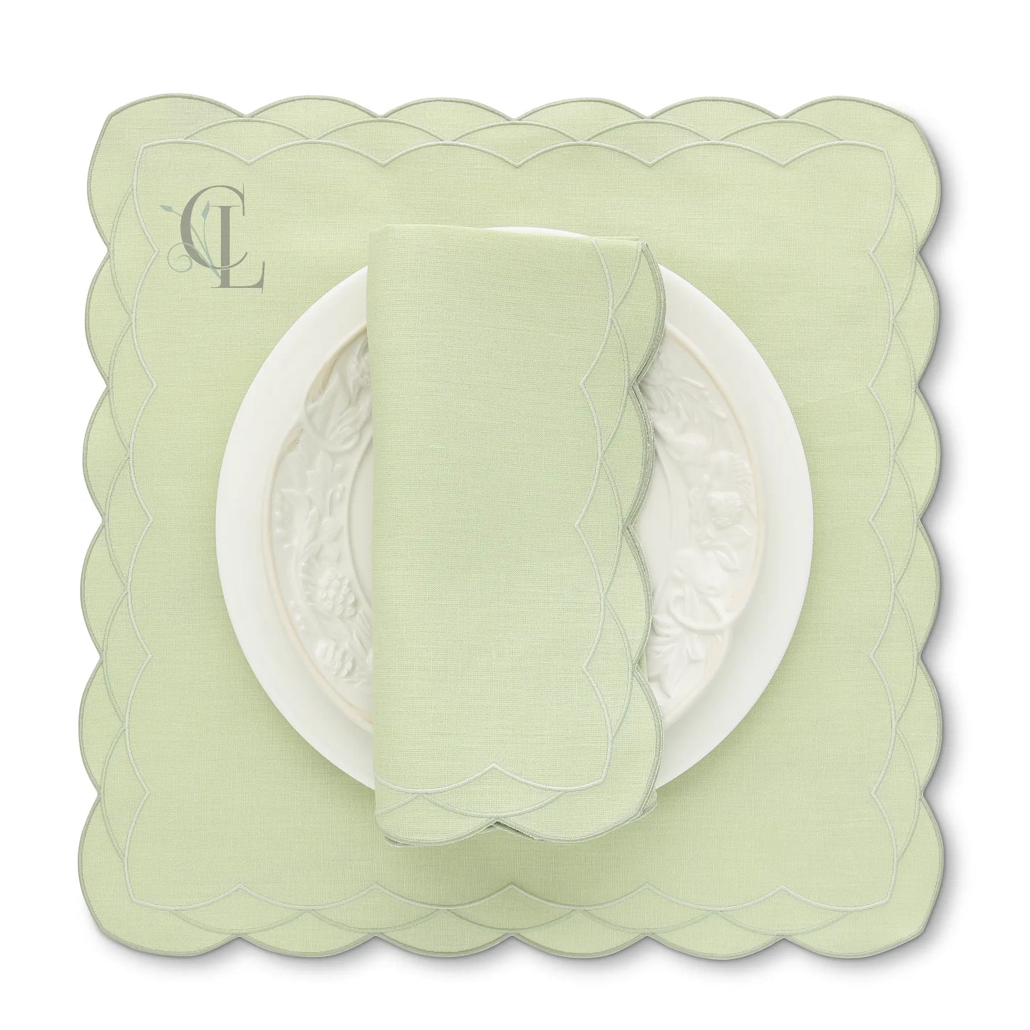 Light green scalloped placemat with a matching napkin on a white background, featuring 'Exclusive cora's Linens' branding.
