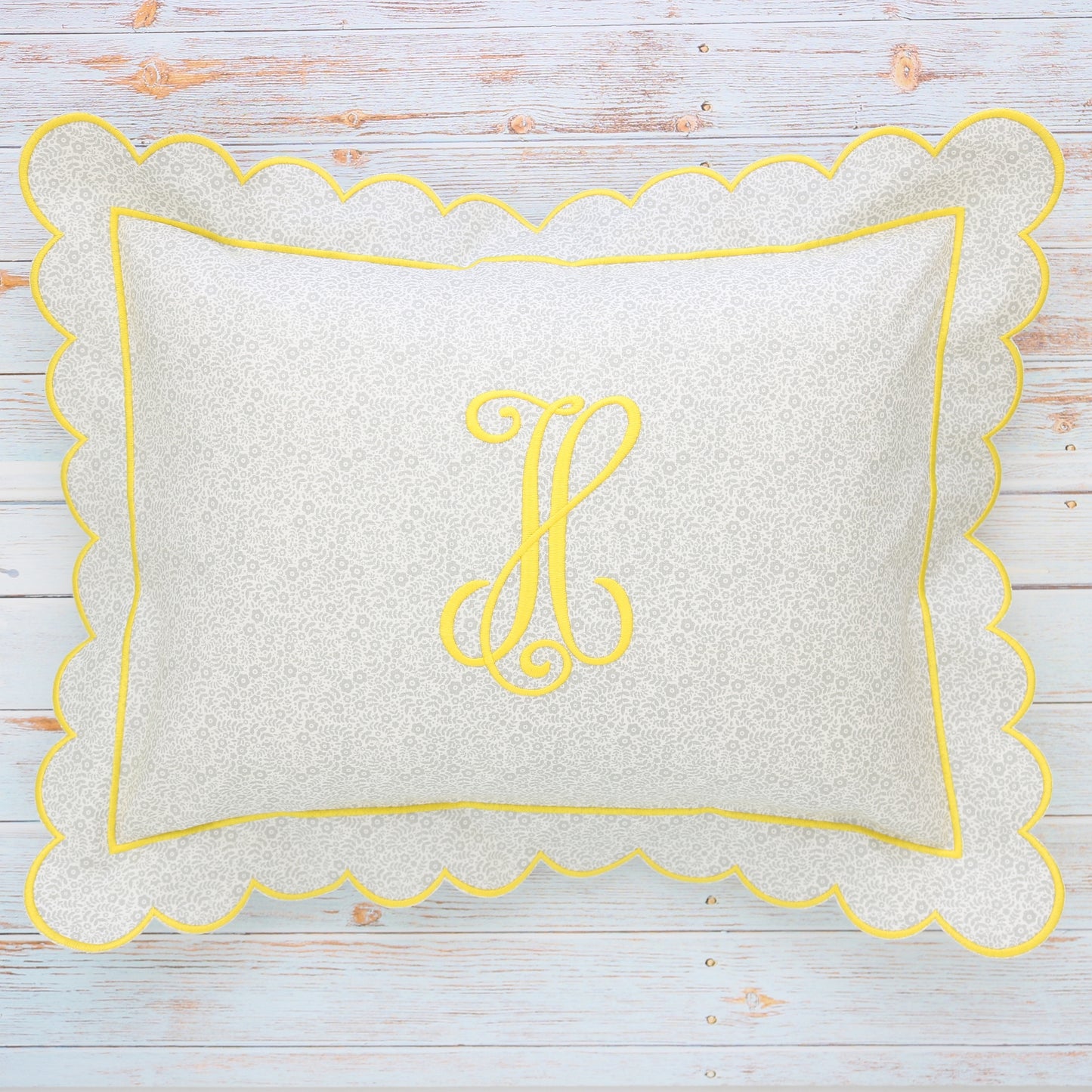 A rectangular boudoir sham with a small floral print and scalloped yellow edge, featuring a monogrammed letter 'H' in the center.