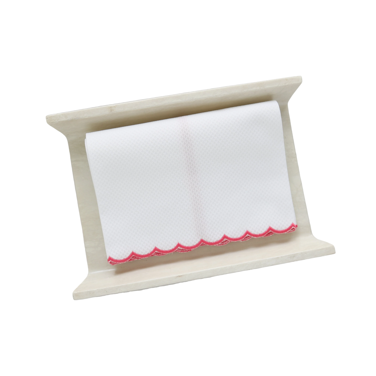 A white pique fingertip towel with fuchsia scalloped edge, folded to fit on a cream stone towel holder