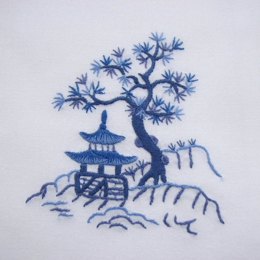 closeup of an embroidered design of a tree and pagoda on a white linen guest towel