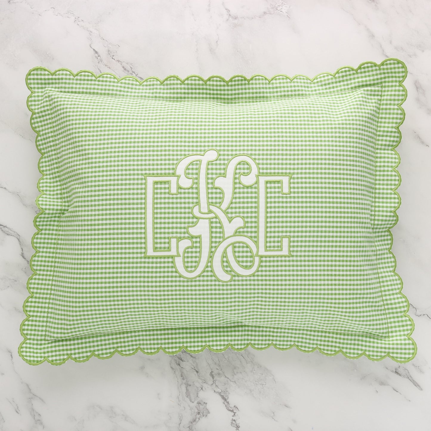 Green and white seersucker scalloped boudoir sham with monogram CKC in White on the front, placed on a marble surface.