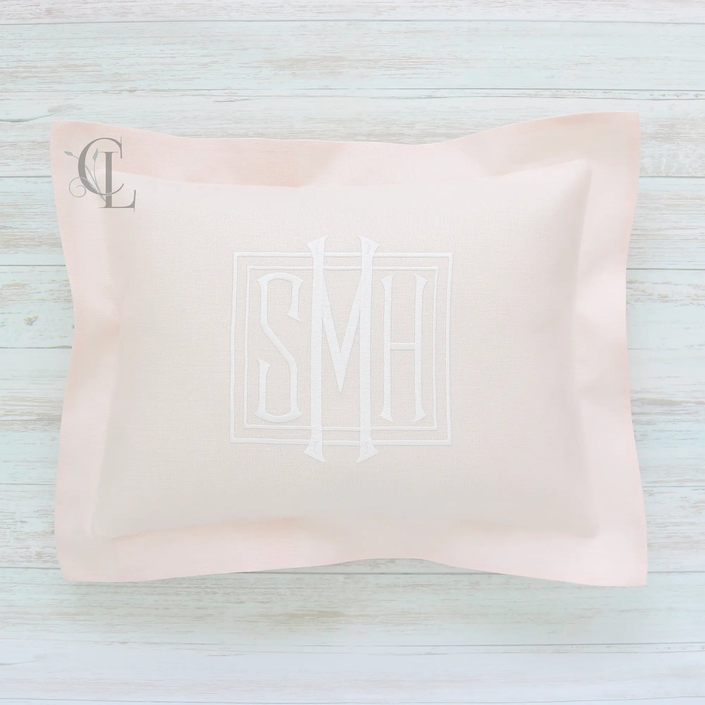 Pink pillow with monogram SMH on a light wooden surface