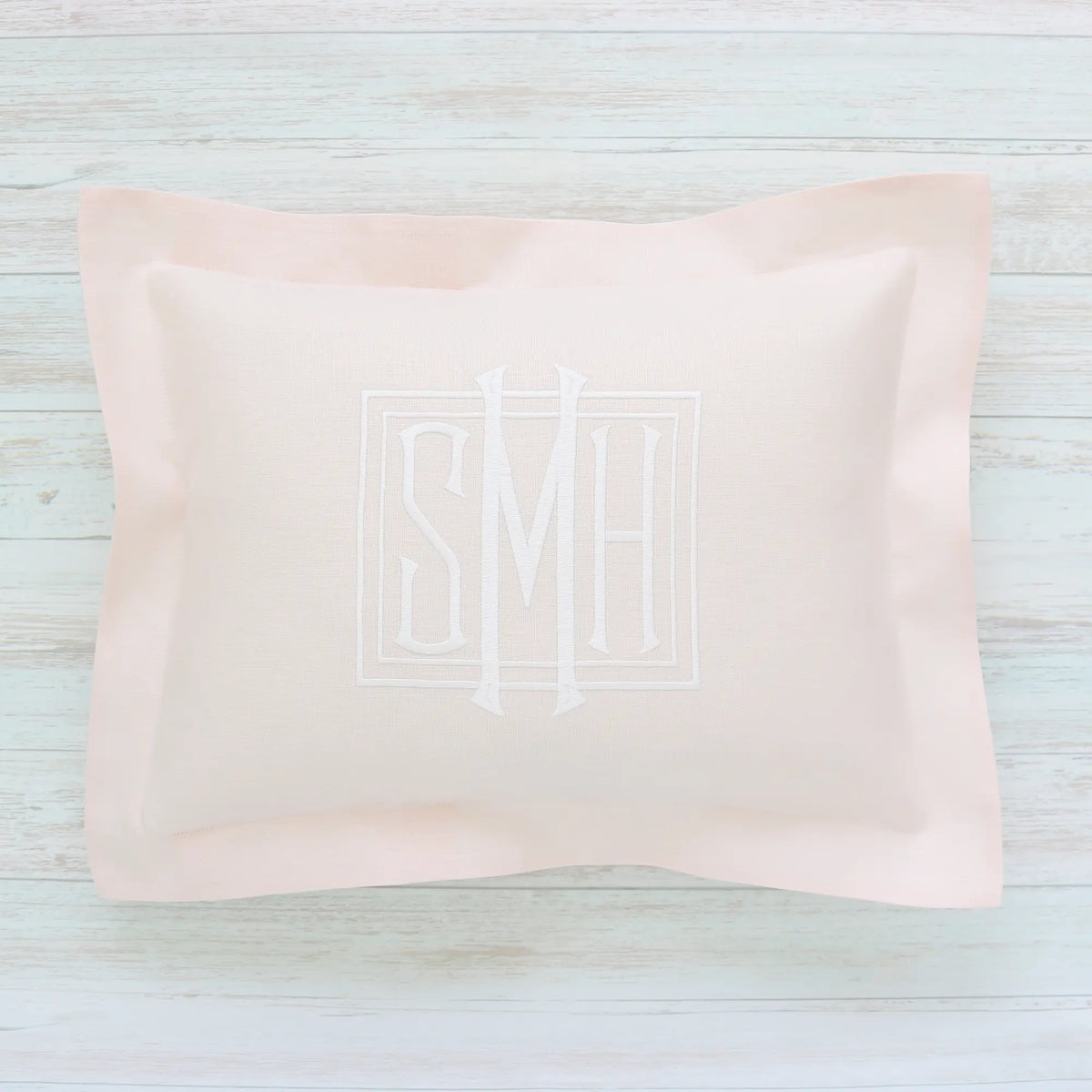 Pink pillow with monogram SMH on a light wooden surface