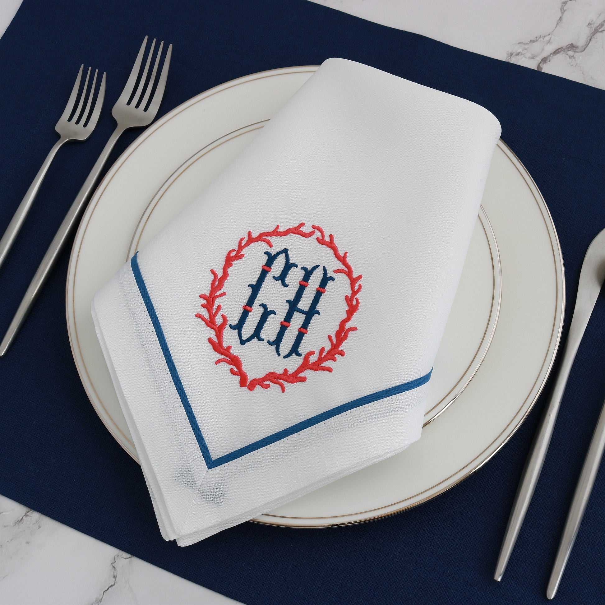 Coral frame embroidery motif and initials CH on a White linen dinner napkin with Cobalt Blue tape trim