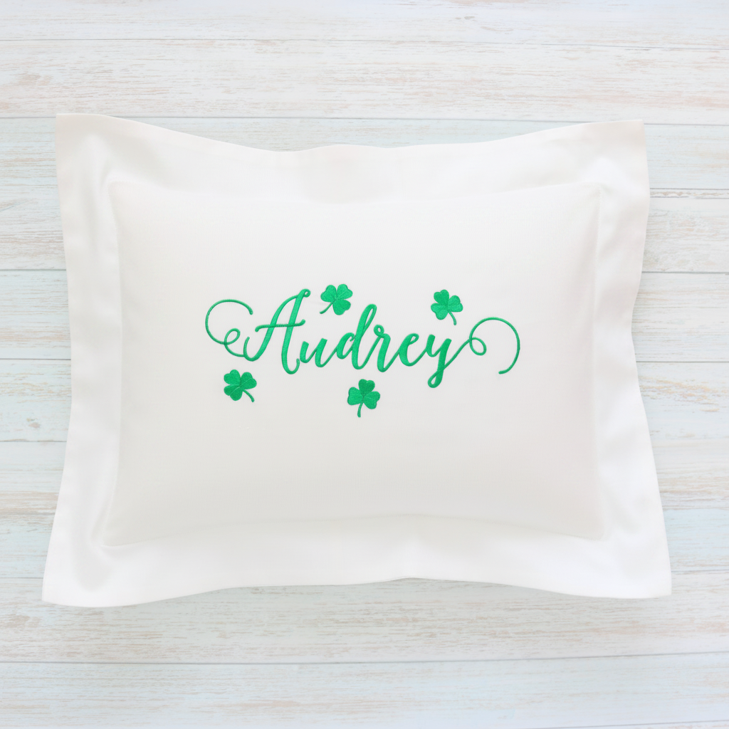 A rectangular white pillow sham featuring the name 'Audrey' in green cursive script with four green shamrocks