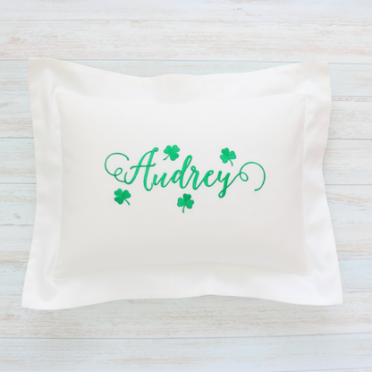 A rectangular white pillow sham featuring the name 'Audrey' in green cursive script with four green shamrocks