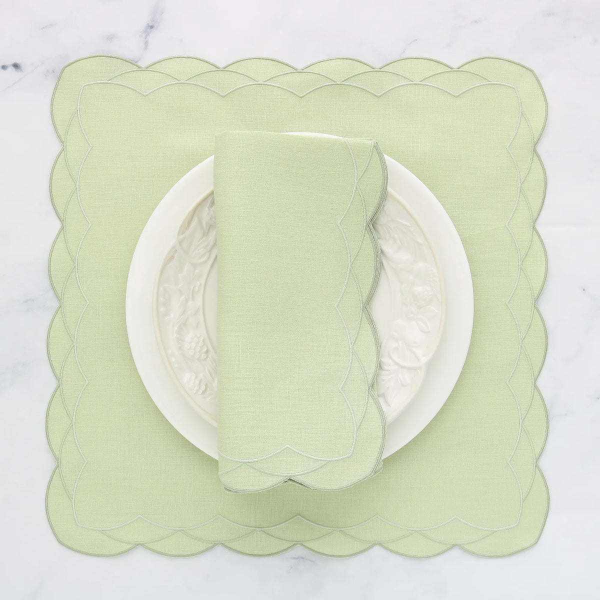 Light green scalloped placemat with a matching napkin on a white background, featuring 'Exclusive cora's Linens' branding.