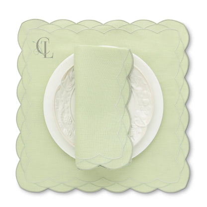 Light green scalloped placemat with a matching napkin on a white background, featuring 'Exclusive cora's Linens' branding.