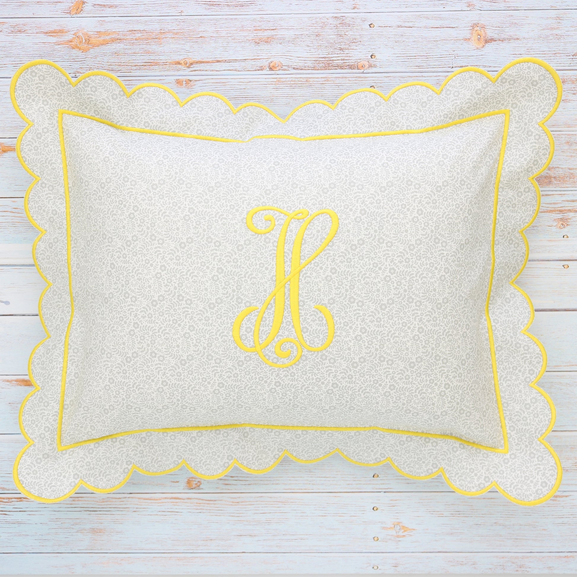 A rectangular boudoir sham with a small floral print and scalloped yellow edge, featuring a monogrammed letter 'H' in the center.