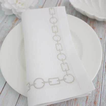 mixed chain motif embroidered in silver metallic on a white napkin, folded on a white plate, handmade by Cora's Linen