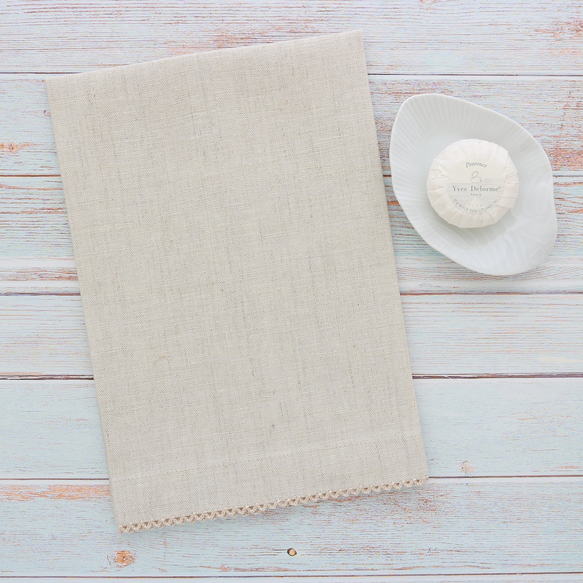 small light oatmeal linen guest towel with natural picot trim next to a soap dish and Yves Delorme round soap