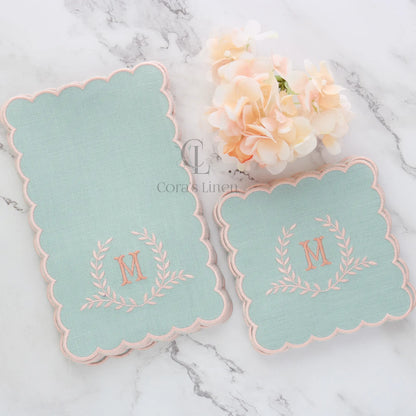 Two sets dusty blue cocktail napkins with peach monogram on a marble surface with flowers, made by Cora's Linen