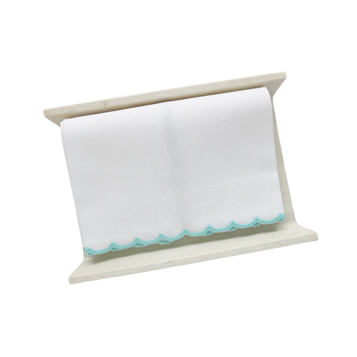 A white pique fingertip towel with an aqua blue scalloped edge, folded to fit on a cream stone towel holder