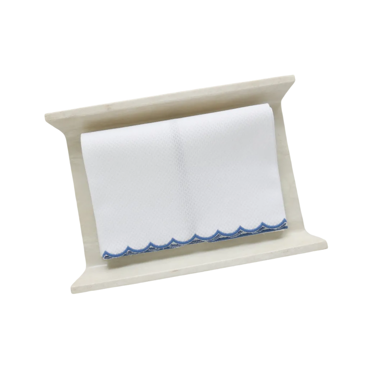 A white pique fingertip towel with a dark blue scalloped edge, folded to fit on a cream stone towel holder