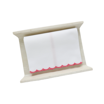 A white pique fingertip towel with fuchsia scalloped edge, folded to fit on a cream stone towel holder