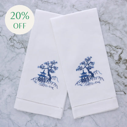embroidered design of a tree and pagoda on two white linen guest towels