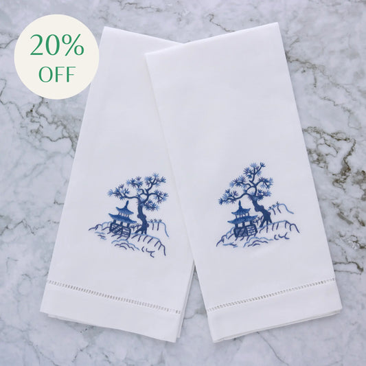 embroidered design of a tree and pagoda on two white linen guest towels