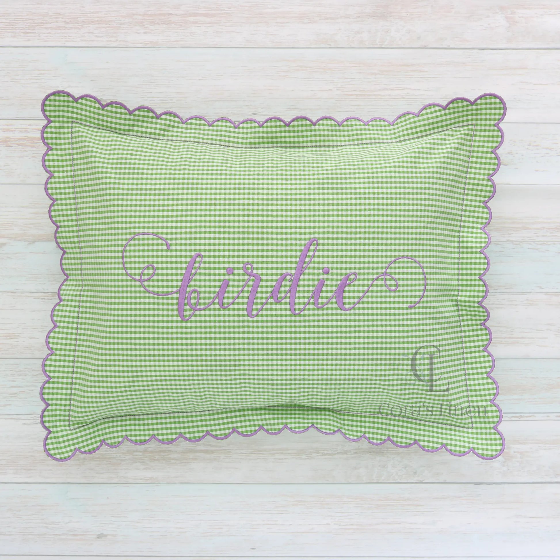 A green and white seersucker cotton fabric boudoir sham with scalloped edges and the name 'birdie' monogrammed in purple.