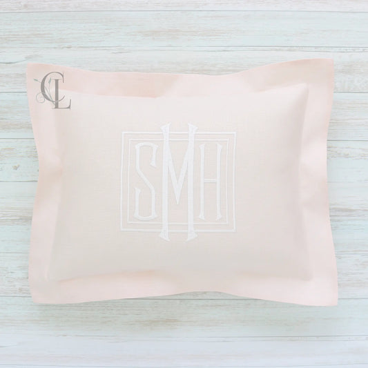Pink pillow with monogram SMH on a light wooden surface